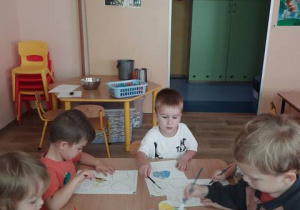 Dziecko siedzą przy stoliku i malują farbami owoce